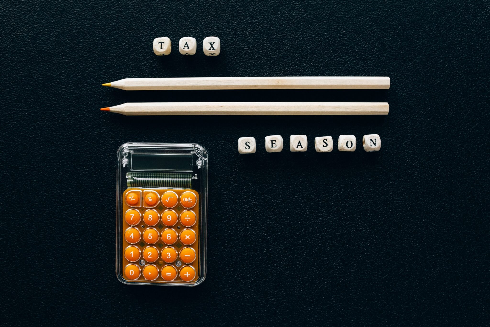 lettered dice spelling “tax season” with pencils and a calculator on a black background