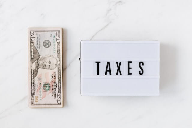 stack of US bills next to a sign saying taxes